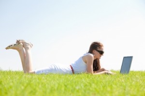 Young Female Lying On The Grass In The Park Using A Laptop